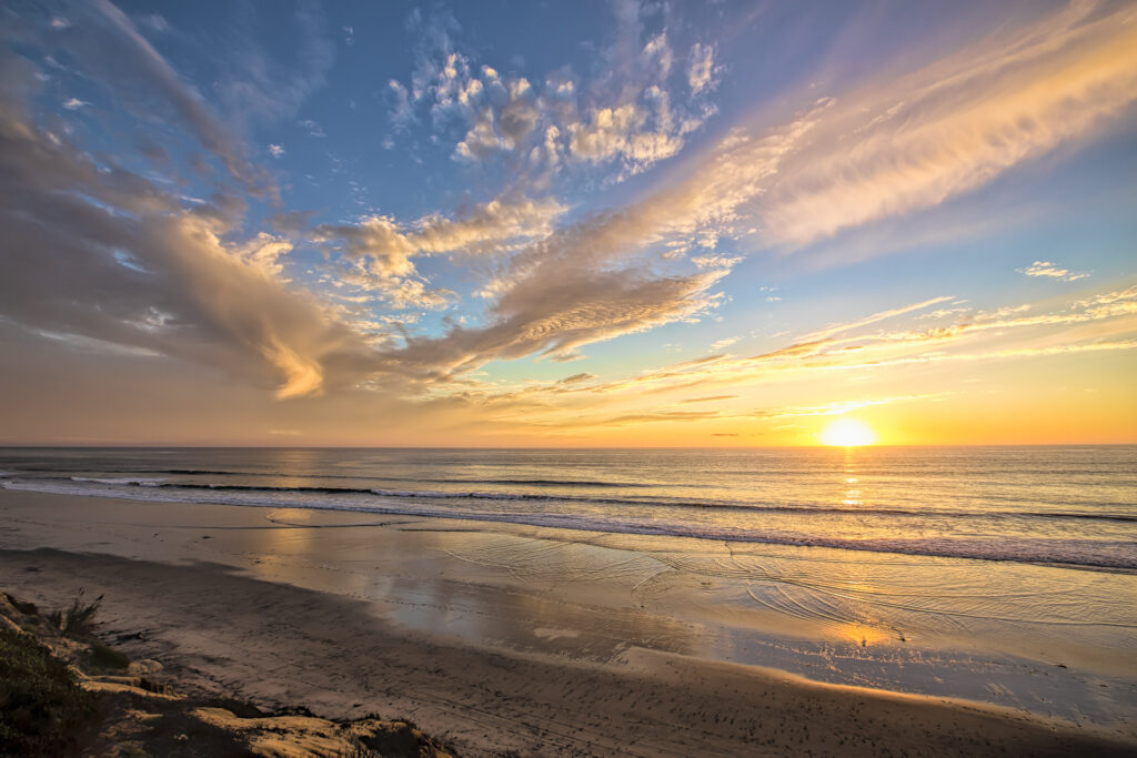 Colorful sunset over a quiet ocean beach with dramatic wispy clouds