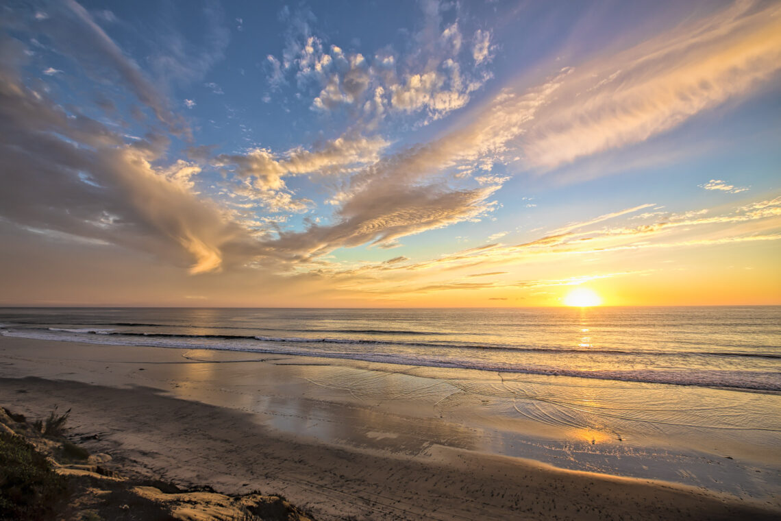 Colorful sunset over a quiet ocean beach with dramatic wispy clouds