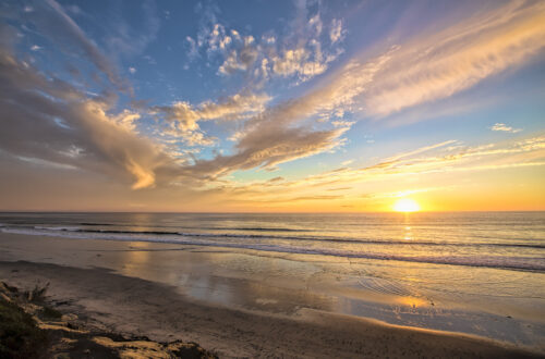 Colorful sunset over a quiet ocean beach with dramatic wispy clouds
