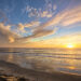 Colorful sunset over a quiet ocean beach with dramatic wispy clouds