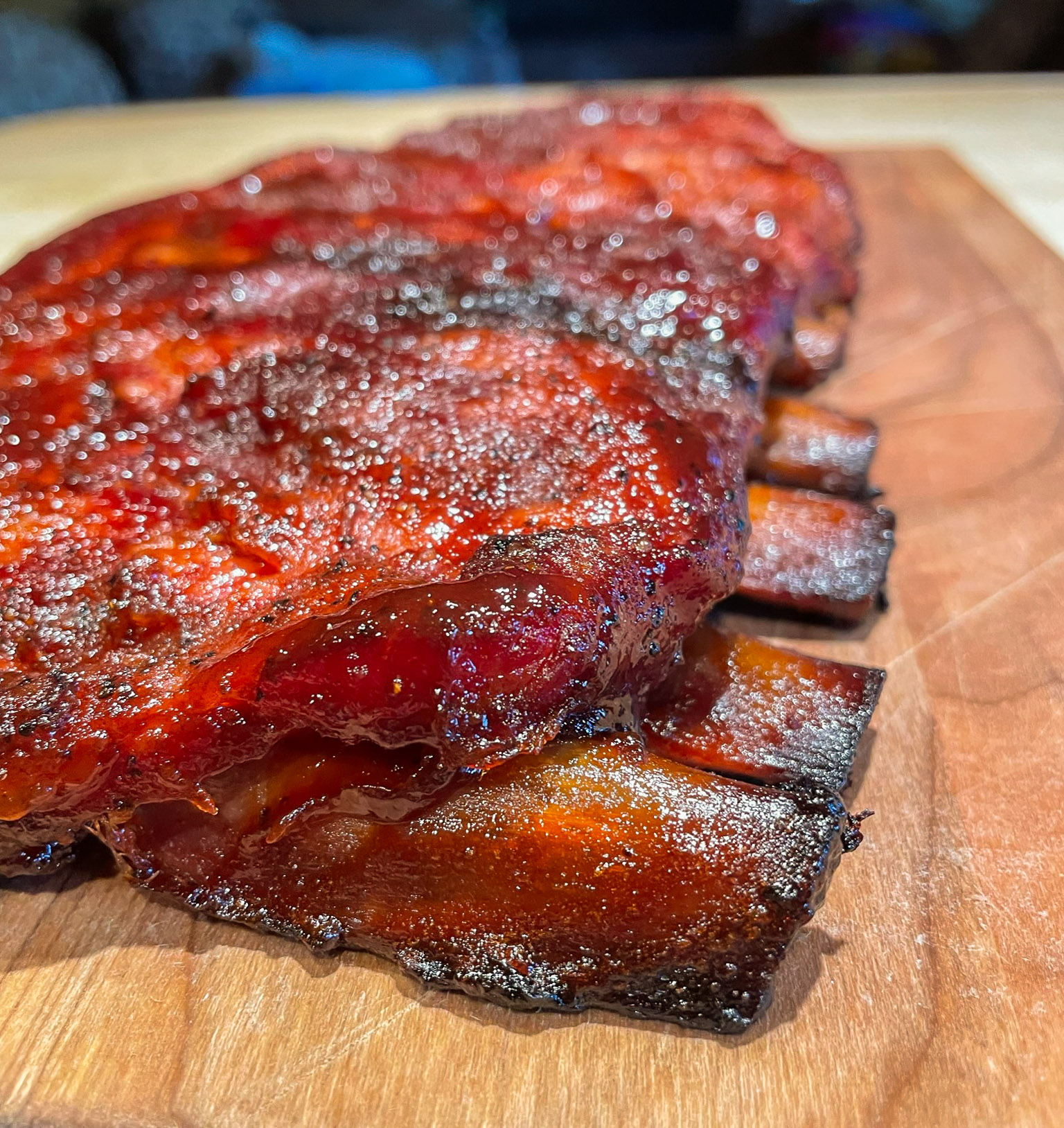 Close‑up of tender barbecue pork ribs with a glossy caramelized glaze on a wooden cutting board, highlighting rich smoky texture and golden‑brown char.