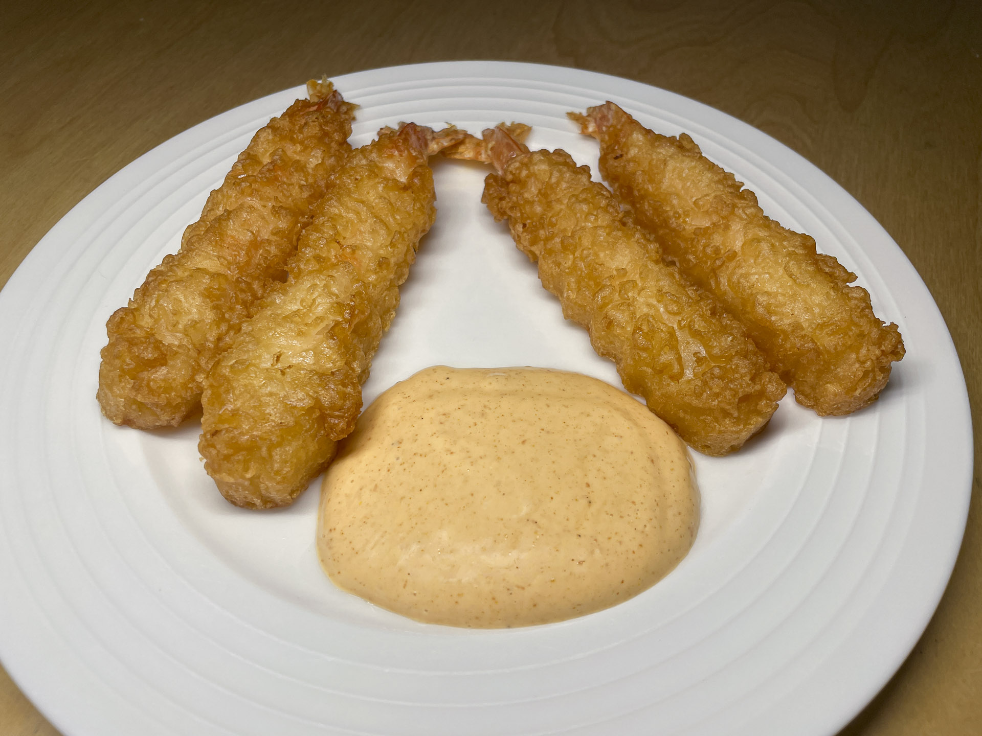 Crispy golden tempura shrimp served on a white plate with creamy spicy dipping sauce, perfect for seafood appetizers.
