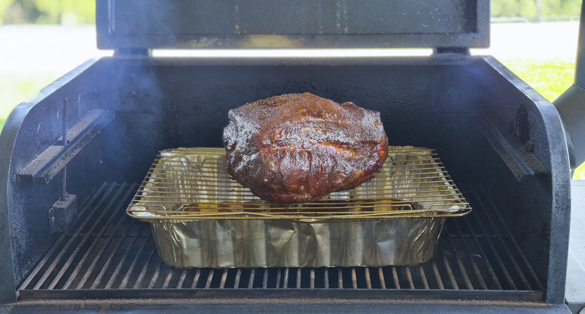 Smoked pork shoulder cooking inside a barbecue smoker, resting on a metal rack above a foil pan with visible smoke and caramelized bark.Smoked pork shoulder cooking inside a barbecue smoker, resting on a metal rack above a foil pan with visible smoke and caramelized bark.