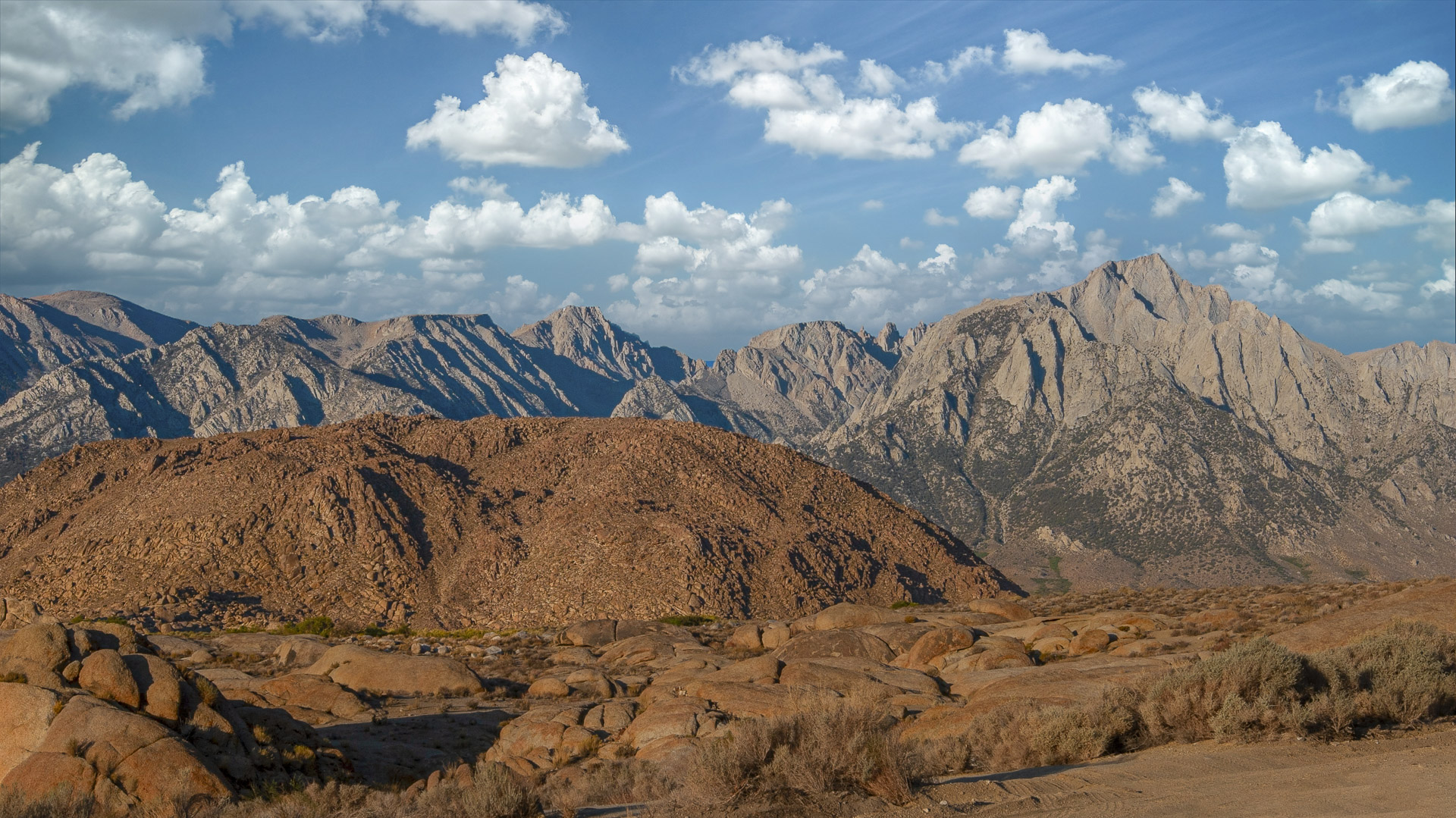 Rounded granite boulders and rugged Sierra Nevada peaks beneath a blue sky in the Alabama Hills near Lone Pine, California.