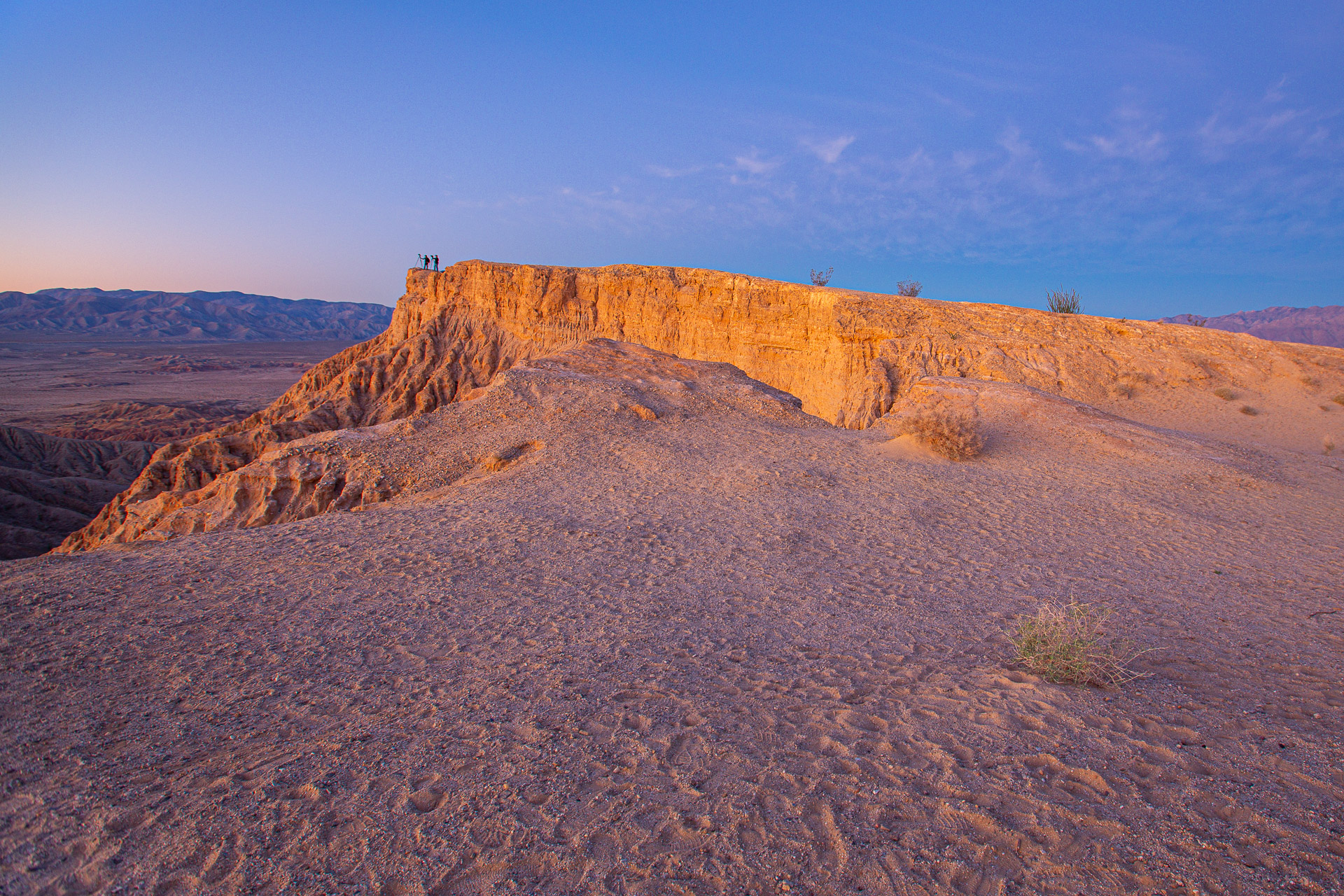 Early morning sunlight illuminates the golden cliffs of Fonts Point in Anza-Borrego Desert State Park, with photographers silhouetted against the sky.