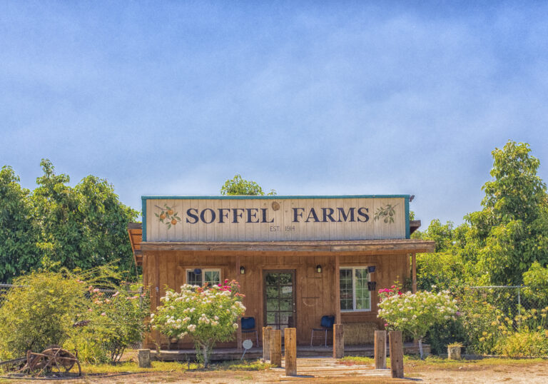 Rustic wooden Soffel Farms building in Redlands, surrounded by flowering shrubs and fruit trees.
