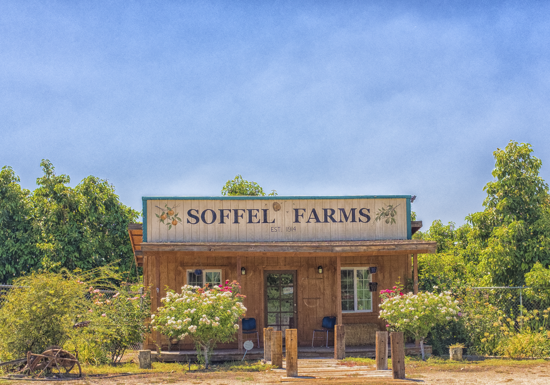 Rustic wooden Soffel Farms building in Redlands, surrounded by flowering shrubs and fruit trees.